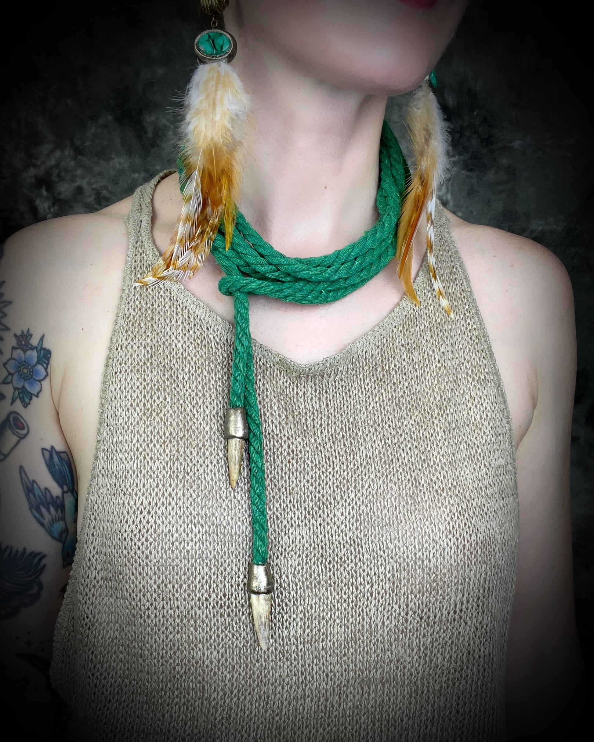 A person wearing a beige tank top adorned with a green rope necklace featuring antler tips and small quartz points.