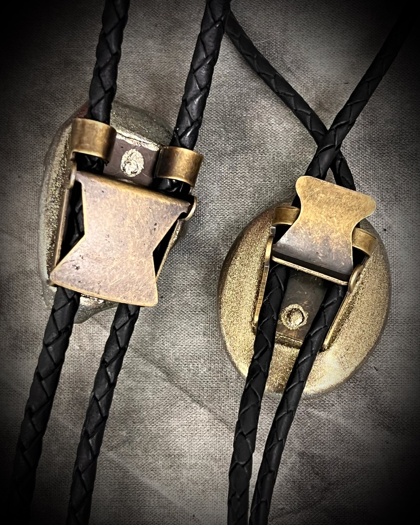 Two bolo ties with brass clasp on a textured gray background