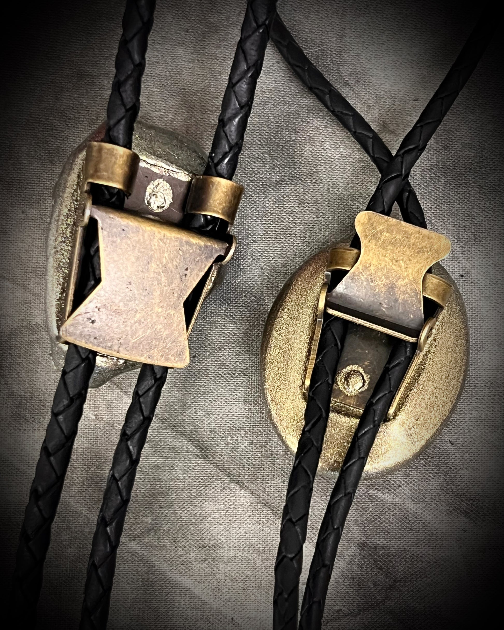 Two bolo ties with brass clasp on a textured gray background