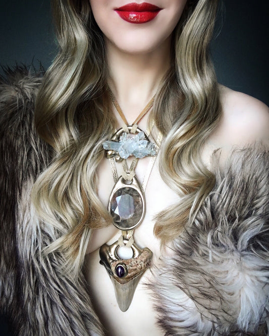 Model wearing layered crystal and shark tooth statement necklaces with gold-tone settings